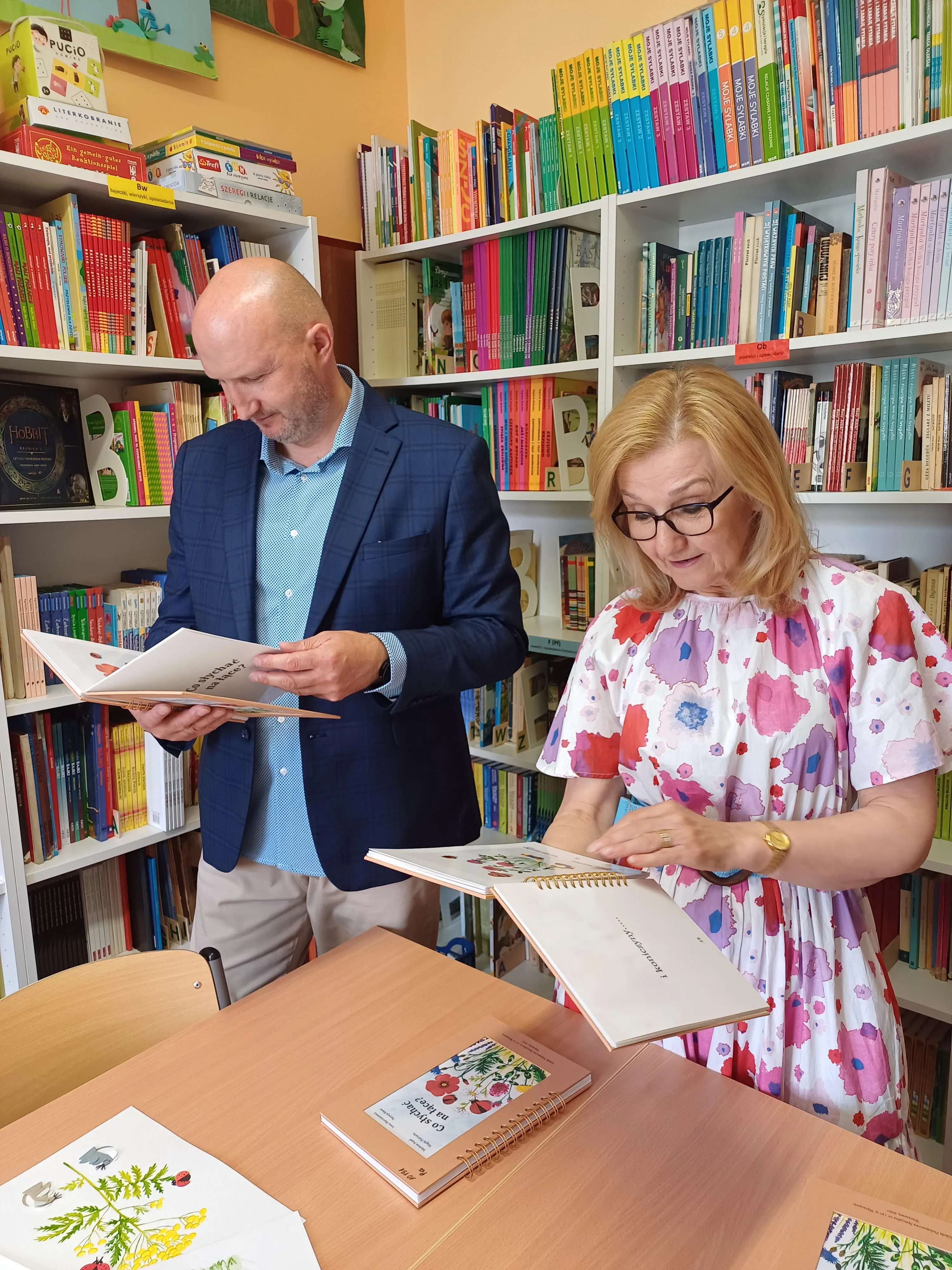Pan dyrektor wraz z panią wicedyrektor oglądają w bibliotece szkolnej egzemplarz książki "Co słychać na łące"