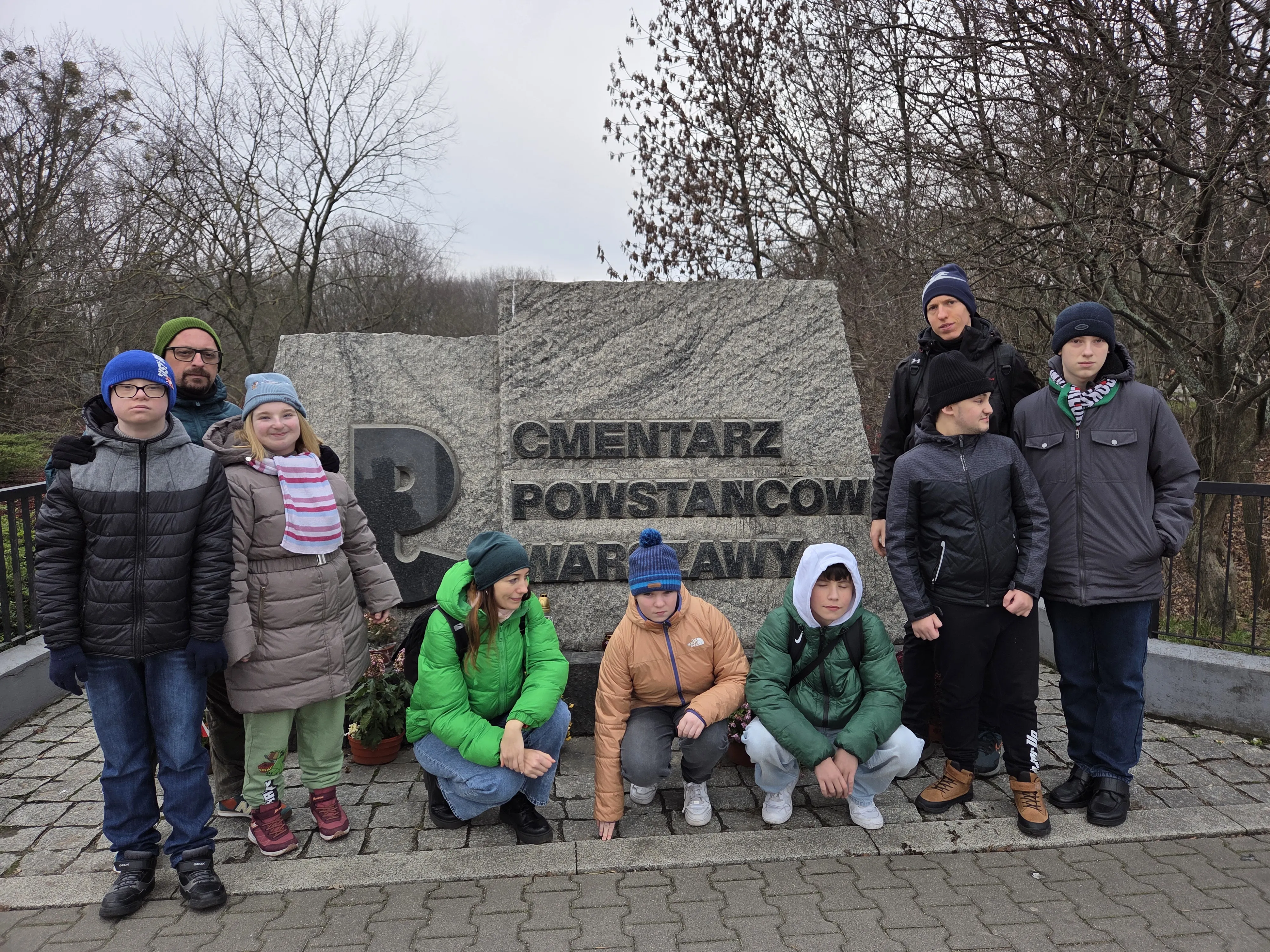 Grupa 6 uczniów i 3 nauczycieli pod  pomnikiem  z napisem : Cmentarz Powstańców Warszawy z 