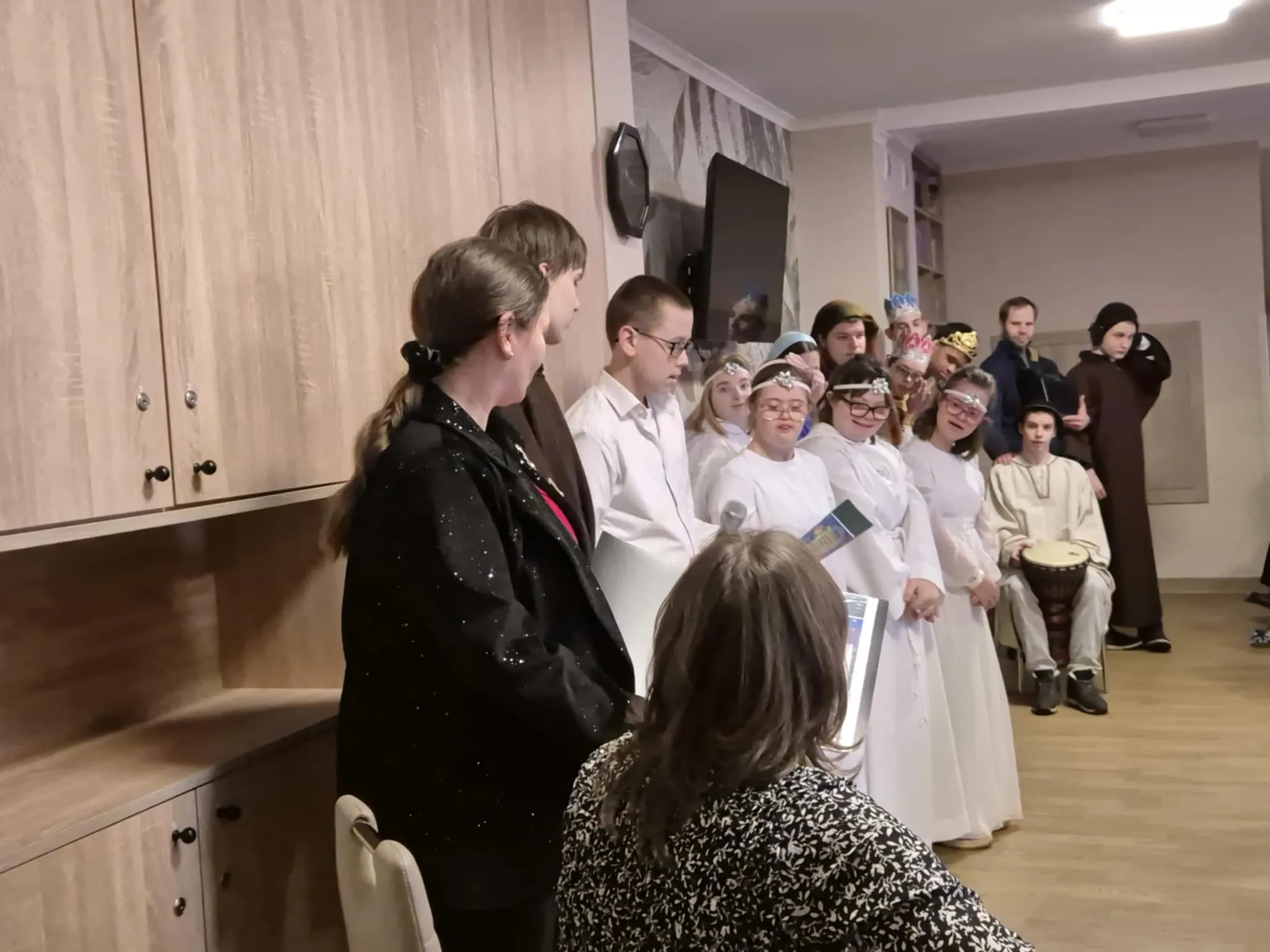 Fragment występu uczniów w zakładzie opiekuńczym. Uczniowie przebrani są za postacie  związane z narodzeniem  Jezusa.  Z prawej strony zdjęcia siedzi pani katechetka z gitarą oraz stoi  jedna z pan wychowawczyń szkoły.