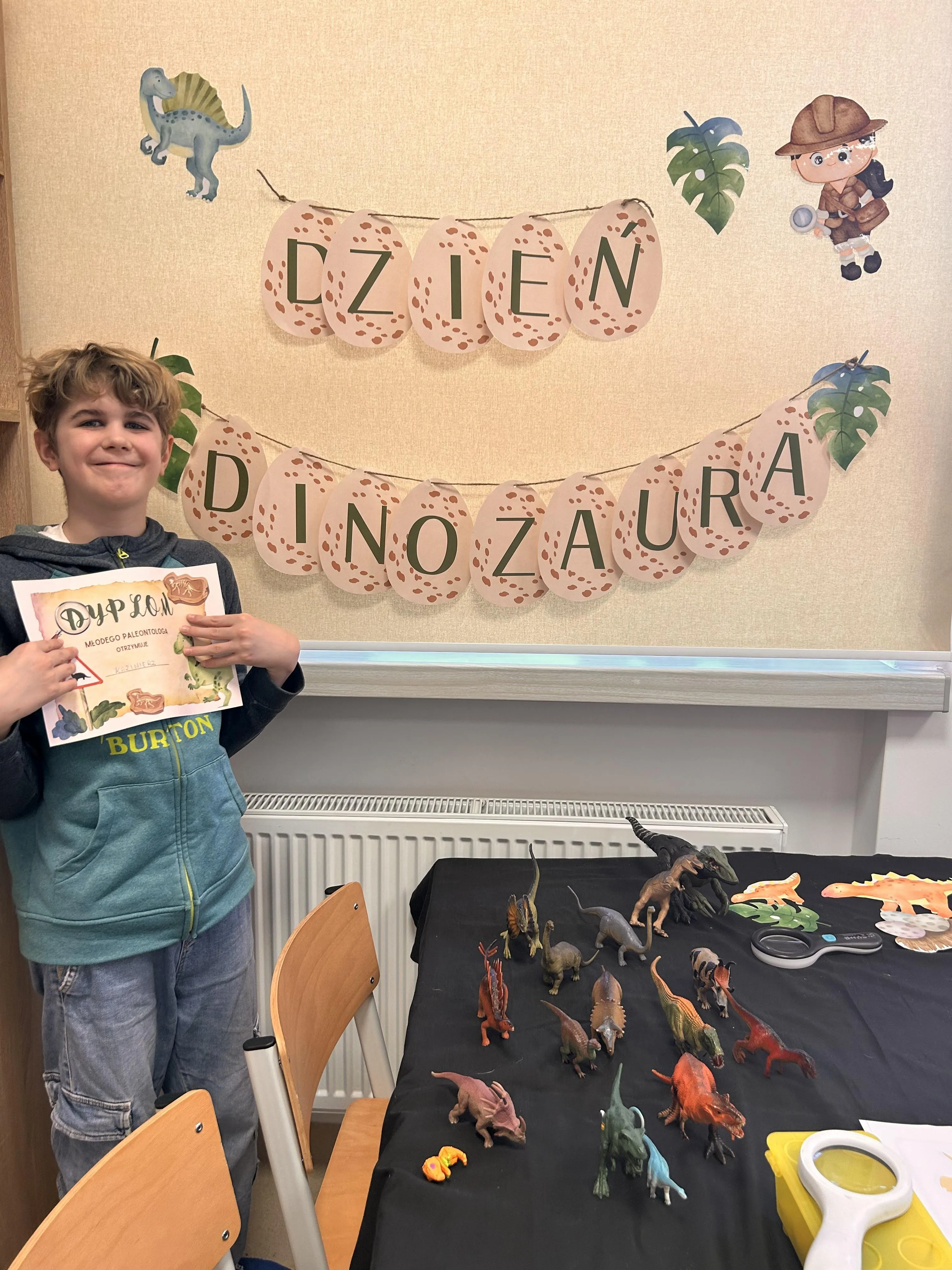 Na zdjęciu uczeń prezentuje dyplom dla młodego paleontologa