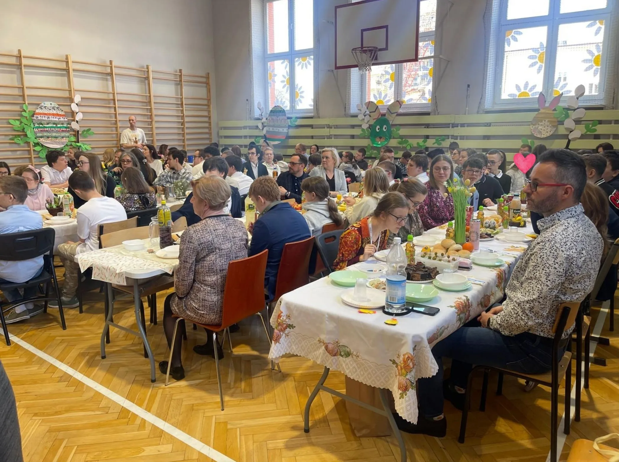 uczniowie i nauczyciele siedzacy przy stołach w sali gimnastycznej przy śniadaniu wielkancnym